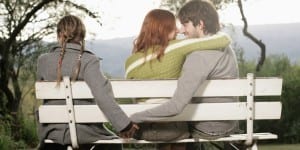 Couple embracing on bench, while man holds other woman's hand